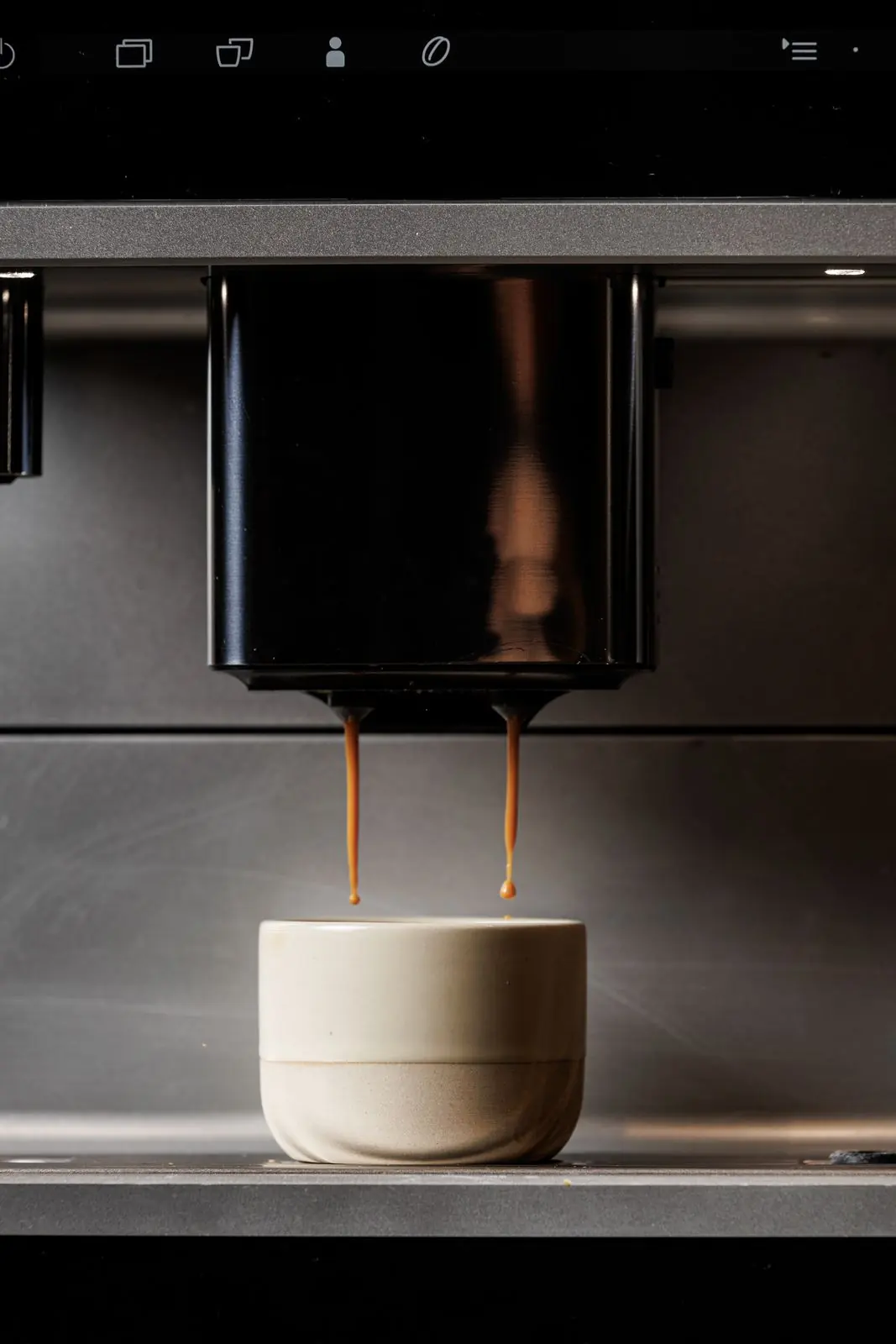 Espresso που πέφτει σε κεραμικό φλιτζάνι από εντοιχισμένη μηχανή καφέ